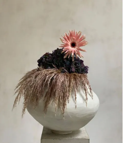 Paris based Castor flowers arrangement with single pink flower amongst dark blue and light purple hay in white vase