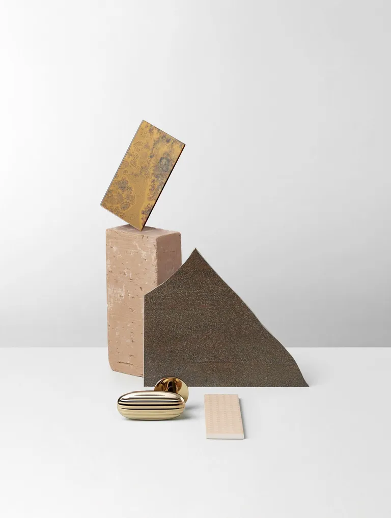 Design Door Handle by Inga Sempé shaped like a madelein in brass, shown next to a composition of bricks and metal sheets