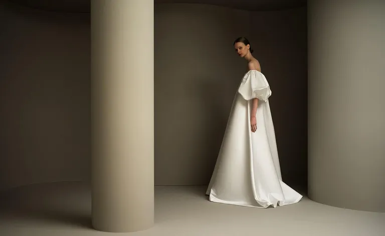 Model wearing off-shoulder white silk wedding gown by In Grid Bride