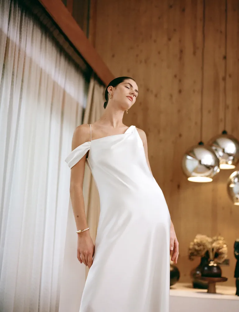 Woman in alternative bridal wear white dress in silk against curtain