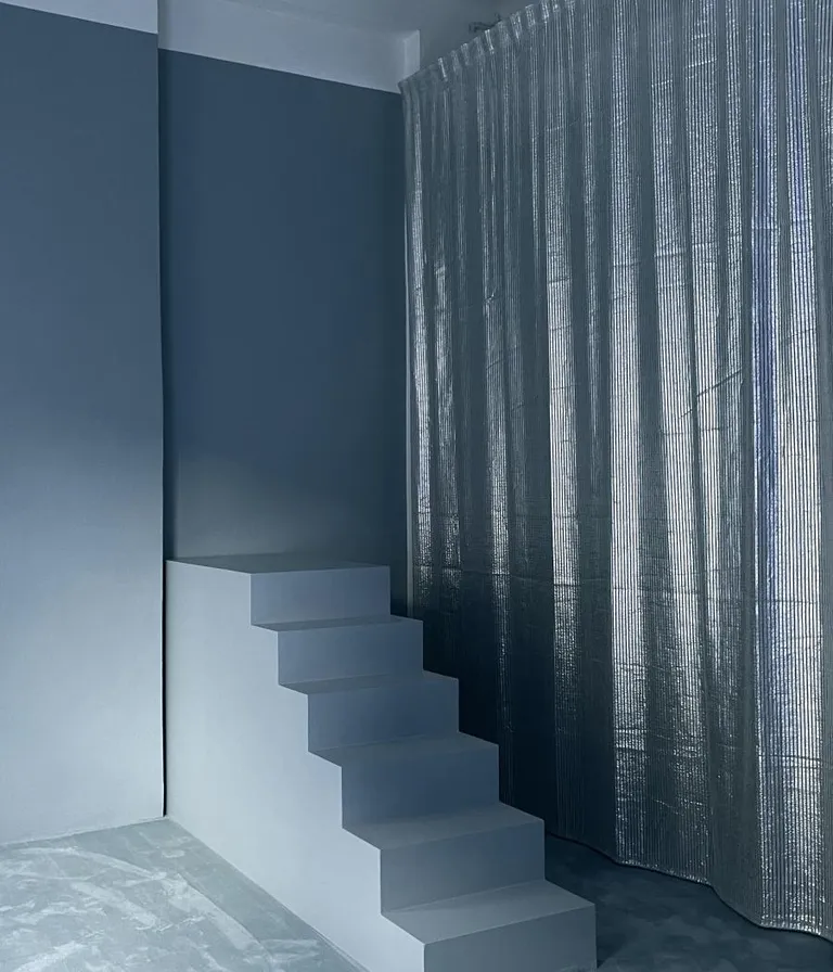 A blue room with staircase and silver curtain at Oxilia gallery